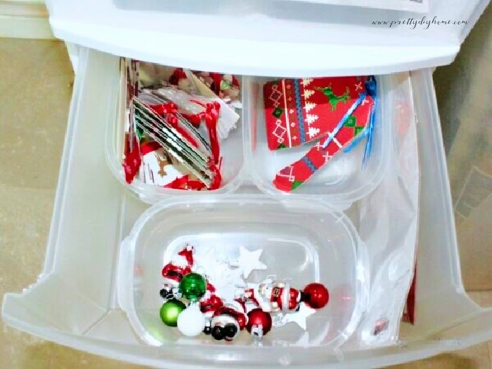 The drawer of a Chrismas wrapping station pulled open showing plastic containers hoding sorted and organized embellishments and tags.