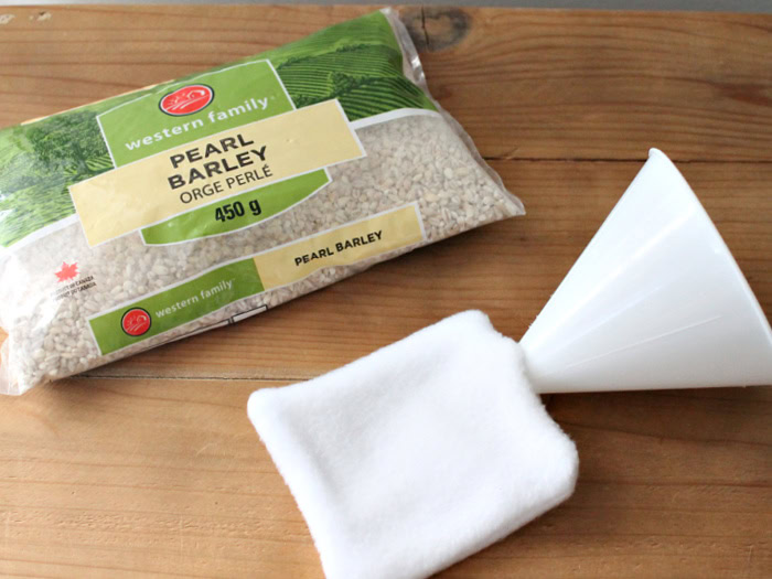 A bag of barley and a partially sewn diy hand warmer with a funnel showing placement of the open section.