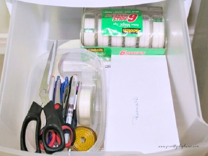 A drawer of a Christmas wrapping station open with containers for pens, envelope marked for receipts and a large package of tape.