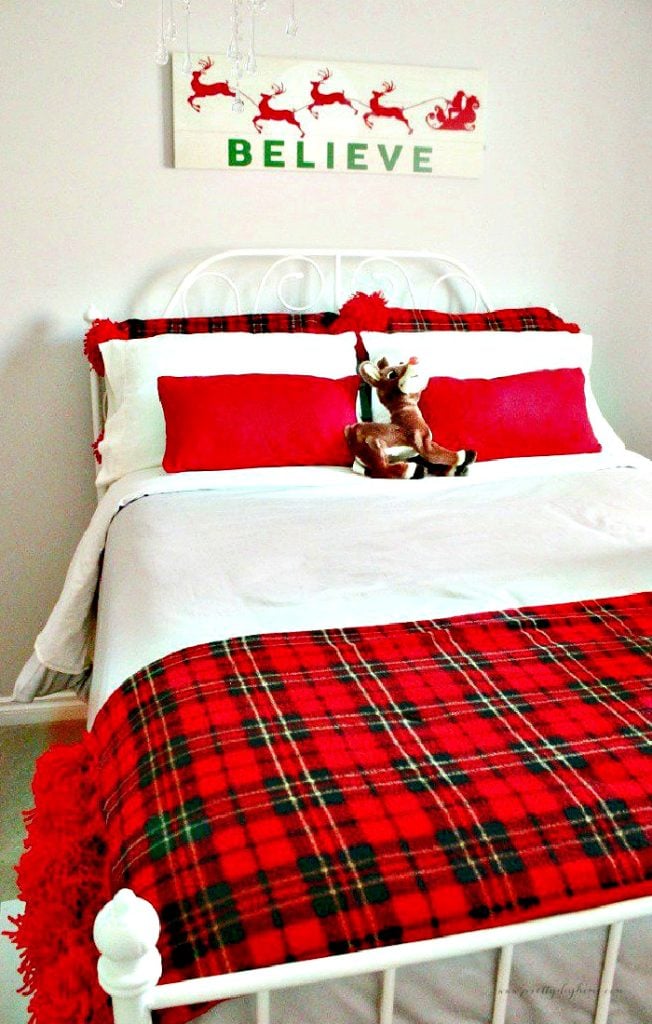 A bed decorated for Christmas with DIY red cushion covers, and a large red DIY tartan bed cover with lots of pom poms.