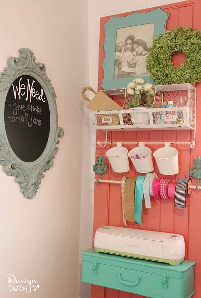 A craft room bing decorated with a door that has several unique shelf ideas attached to it, Wire organizer and a small suitcase with a cricut machineon it.