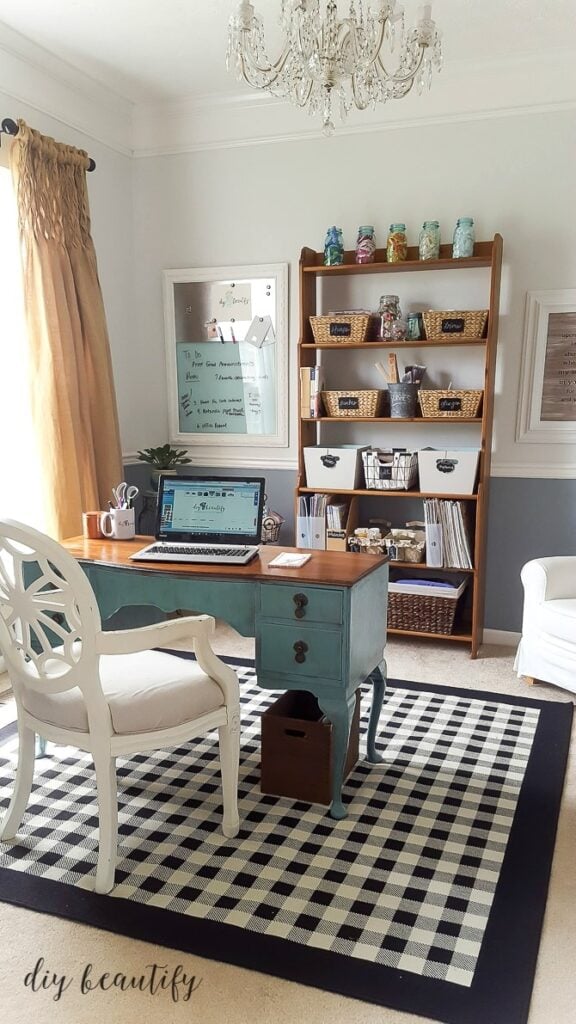An office craft room combination with a beautiful blue desk, antique furniture with baskets and bins and a cozy white chair.