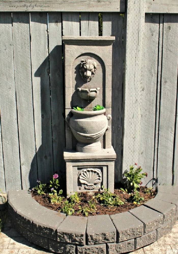 Concrete lion head water fountain surrounded by a small brick flower bed DIY repair tutorial.