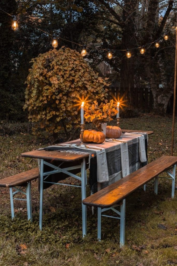 An old refinished outdoor table decorated with a plaid table cloth, pumpkins, candles and beautiful string lights outside in the back yard.