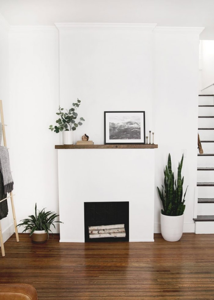 A bright white fireplace with simple wood mantel, the faux firebox is painted black an electric insert.  