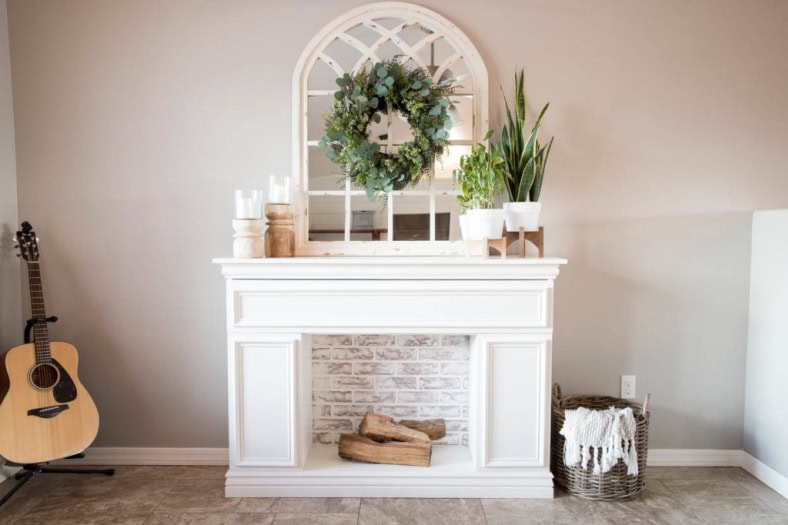 A nice bright white faux fireplace with a mantel. The faux fireplace box is filled with faux bricck backing and three small logs.