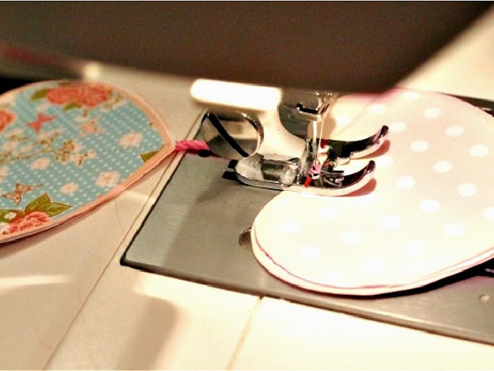 Paper Valentine hearts being sewn onto twine with a sewing machine, showing needle placement and stitching