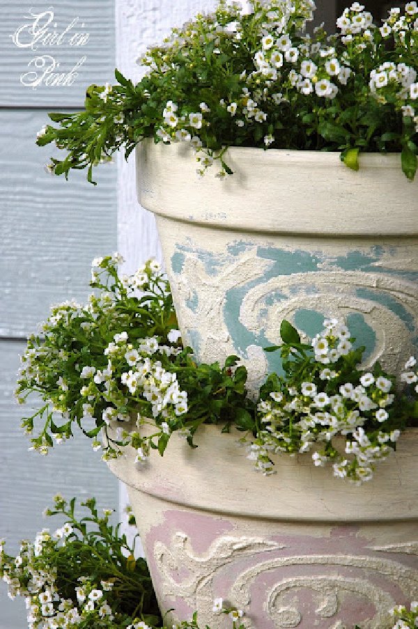 A stacked set of beautifully embossed clay flower pots in soft pastel colors.  The posts are large and are planted with babies breath for outdoors.