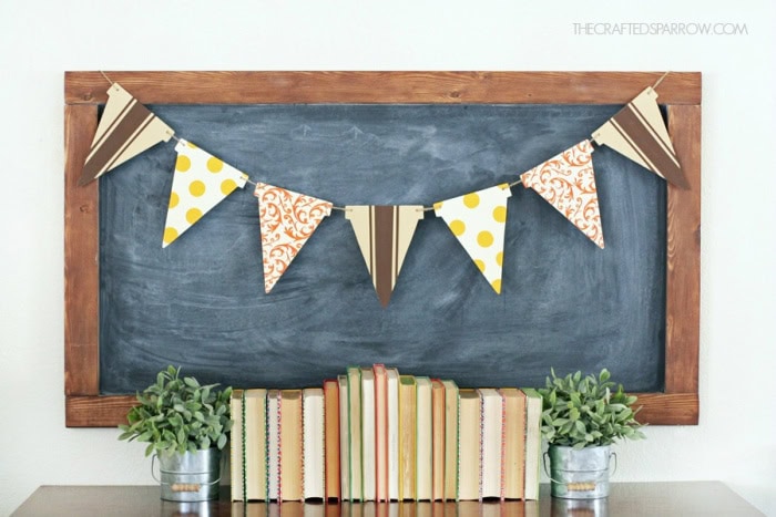 A simple fall banner in soft browns oranges and creams. The banner is made out of wood and is hanging on a chalkboard.