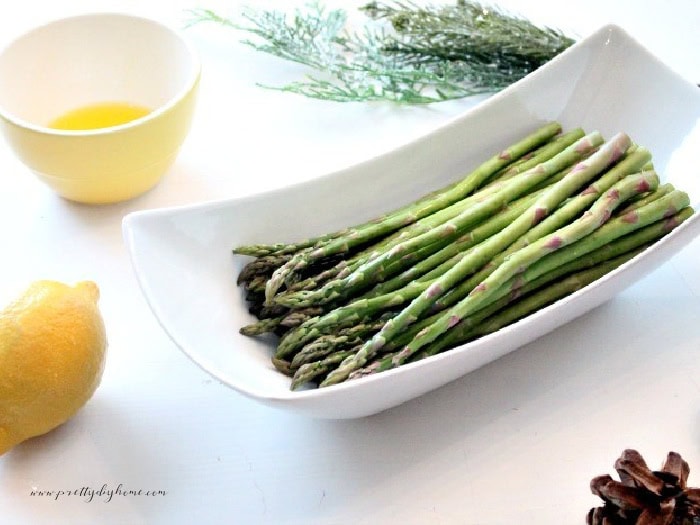 A bowl of clean and trimmed fresh asparagus, a whole lemon, and melted butter in a small yellow bowl waiting to be made into aspragrus phyllo Christmas appetizers.