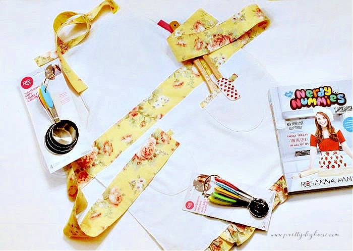 Handmade children’s apron with yellow ties styled with a kids cookbook and colorful baking tools, easy DIY Christmas gift idea