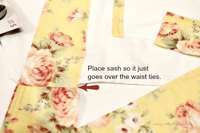 Placing the sash across the front of a handmade children’s apron so it slightly overlaps the waist ties before topstitching