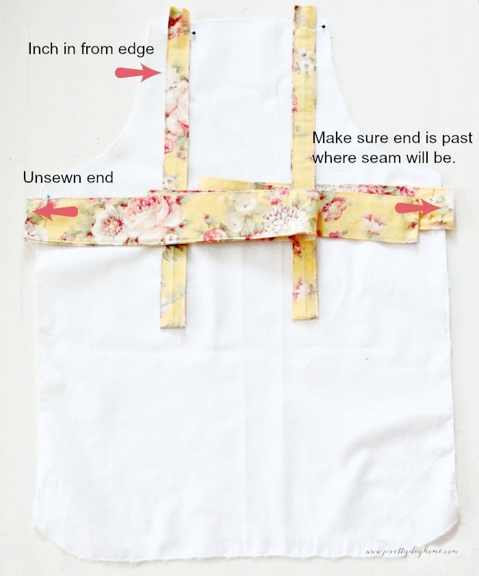 Lower apron piece with neck and waist ties pinned in place showing zigzag finished edges before attaching the second fabric layer