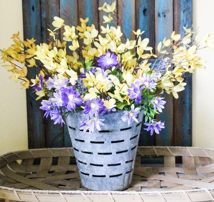 A pretty Spring centerpiece made with forsythia branches and soft purple flowers, inside a vintage olive bucket.