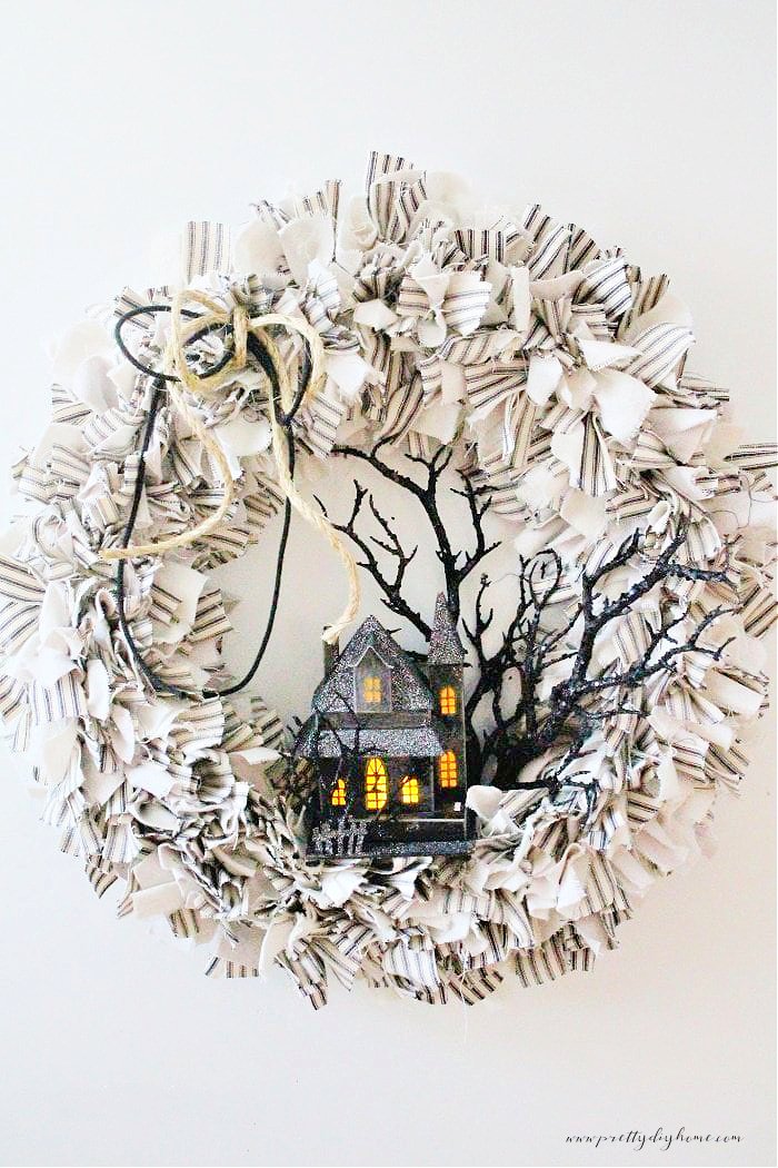 A DIY Halloween rag wreath in neutral colors decorated with a pretty sparkling black haunted house and branches.