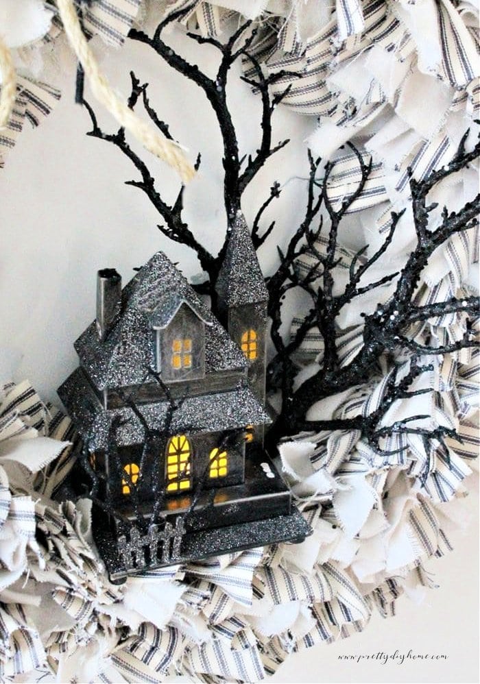 A closeup of a Halloween themed rag wreath showing details of a haunted house and spooky tree.