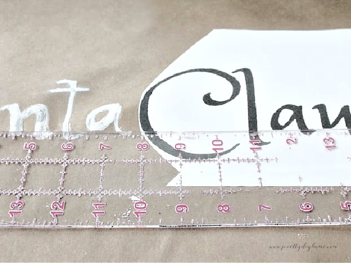 DIY Christmas scroll sign template with Claus on the left and Santa chalk lettering on the right, ruler aligning bottom edges.