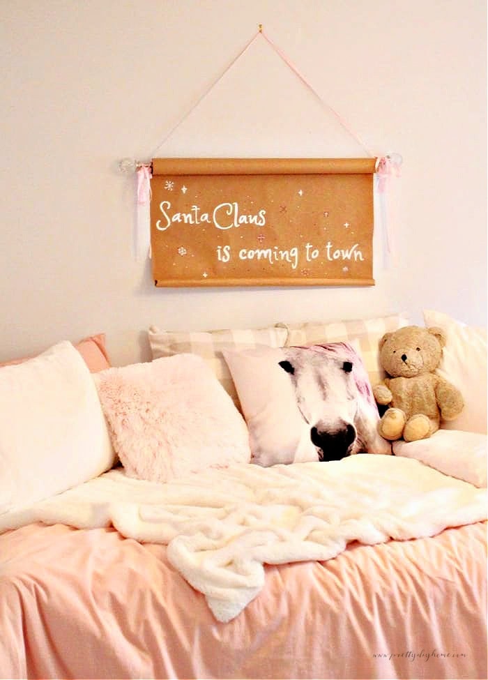 DIY pink Christmas scroll sign hanging above a bed with pink cover, soft fur throw, pink pillows, pony pillow, and vintage grey teddy bear.