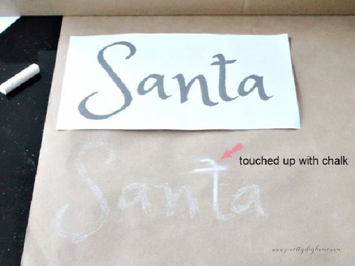 DIY scroll sign template with the word Santa on top and chalk lettering transferred underneath, arrow showing darkened chalk area.