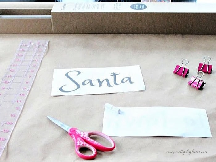 Supplies for making a DIY pink Christmas scroll sign including scissors, ruler, clips, chalk and free printable template.