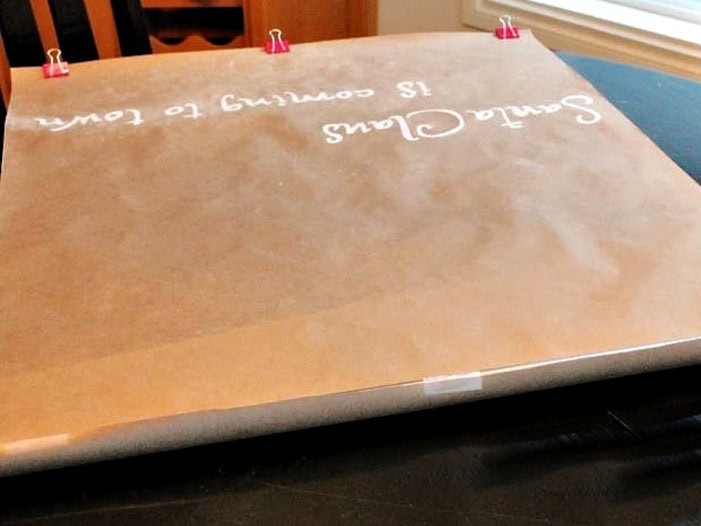 Completed DIY Christmas scroll sign with Santa Claus Is Coming to Town letters traced in white chalk pen.