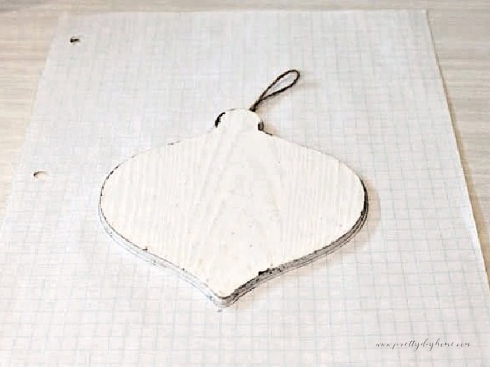 Wooden Christmas ornament placed on graph paper while tracing the outline to make a DIY flannel ornament pattern.