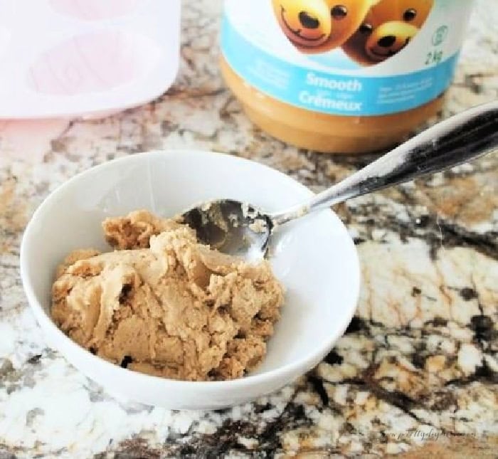 A large bowl filled with peanut butter filling for chocolate Easter eggs, you can see the jar of smooth peanut butter, and the pink Easter egg mold in the background.