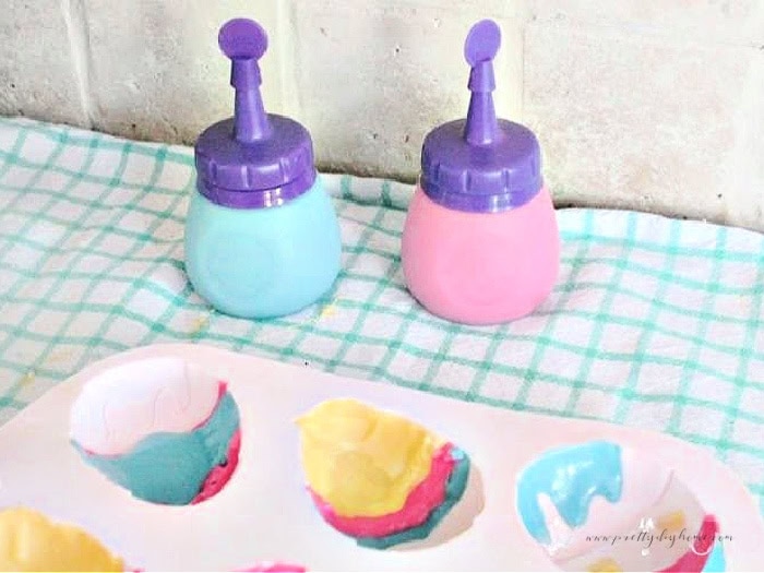 Filling a large chocolate Easter egg mold with colored candy melts.  There are containers for melting the chocolate in the background.