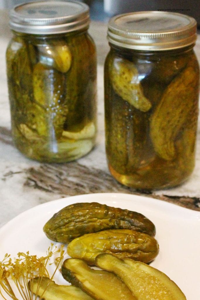 Two jars of homemade dill pickles with slice dill pickles being served in front of them.