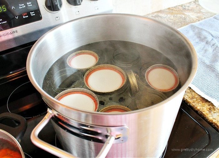 A large pot filled with boiling water, as well as canning jars, rings and lids.