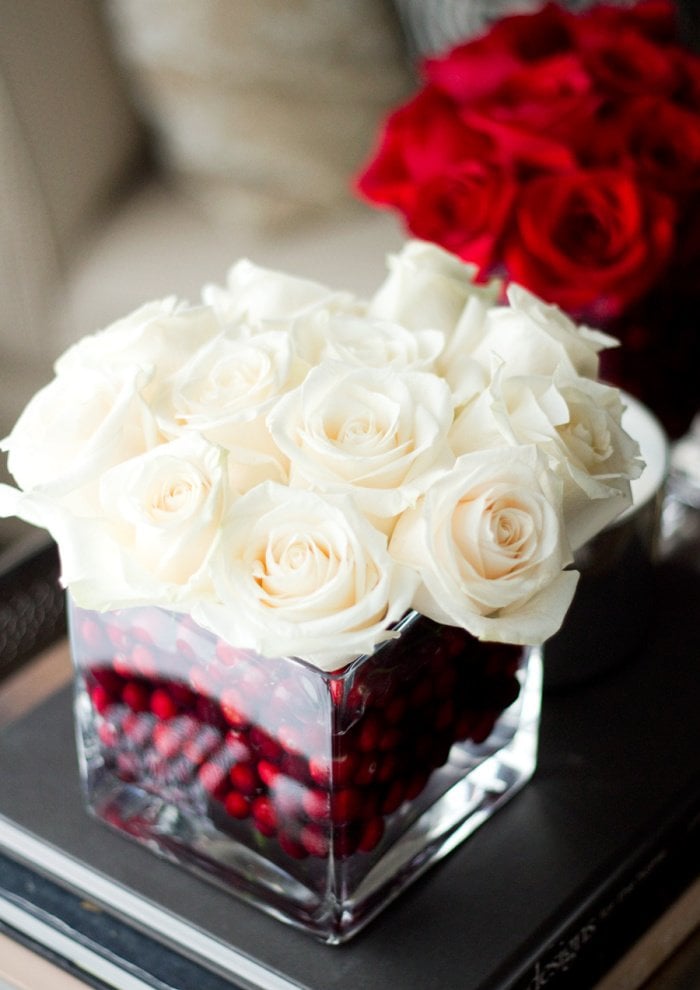 Simple Christmas centerpiece with white roses in a vase filled with red cranberries.