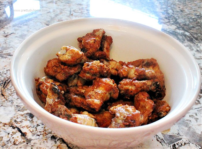 Coating baked chicken wings in a hot and sweet sauce before serving.