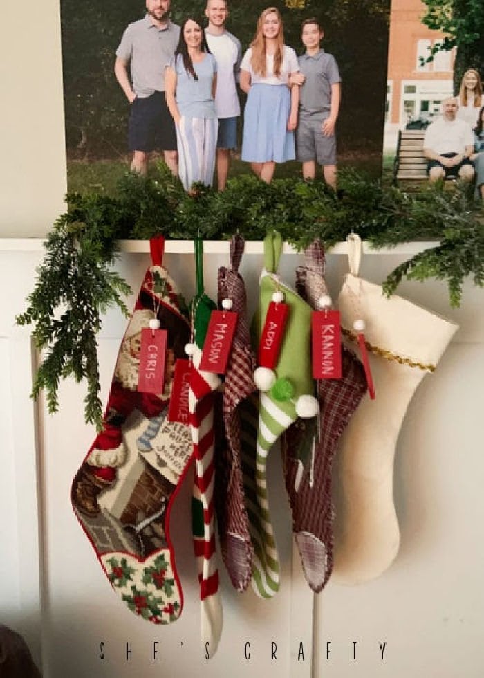 DIY Stocking Name Tags hanging with stockings on a Christmas shelf.