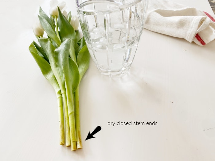 A bundle of tulips waiting for preparation, and a vase full of ice water for the tulips.