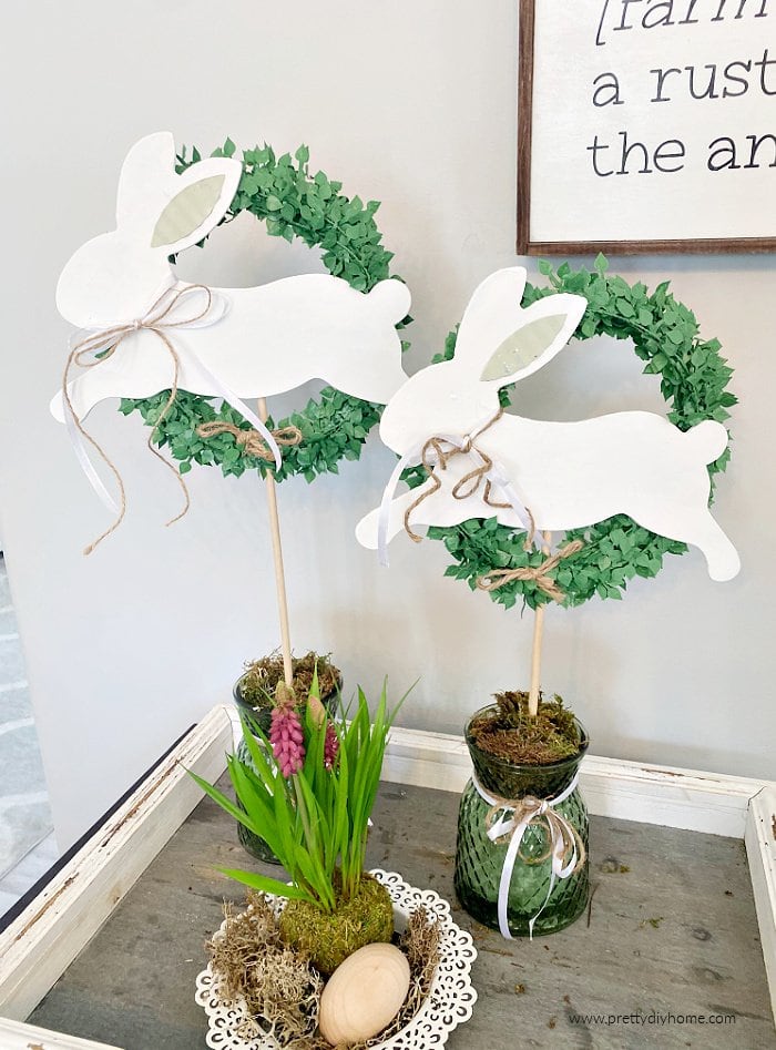 Two wood Easter bunny crafts made using dollar store Easter bunnies. These Easter bunny topiaries are sitting on a tray in a dining room.