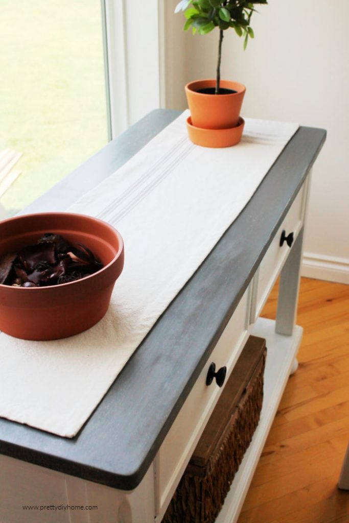 A refinished hallway table with a greige top and white painted sides. The table has a farmhouse runner on top.