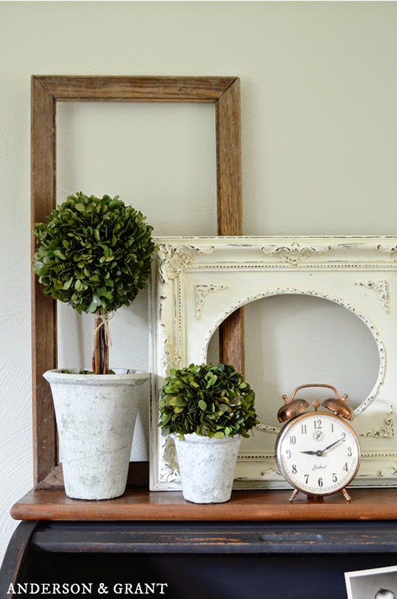 A farmhouse vignette created with two thrifted frames a tall brown one, and a smaller white frame. They are a backdrop to potted plants