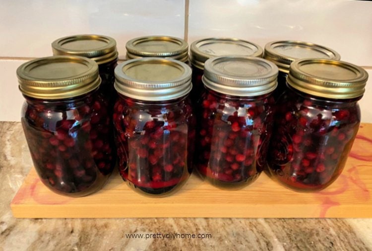 Eight Jars of homemade saskatoon sauce or syrup. The jars are sitting on a wooden cutting board while they cool.