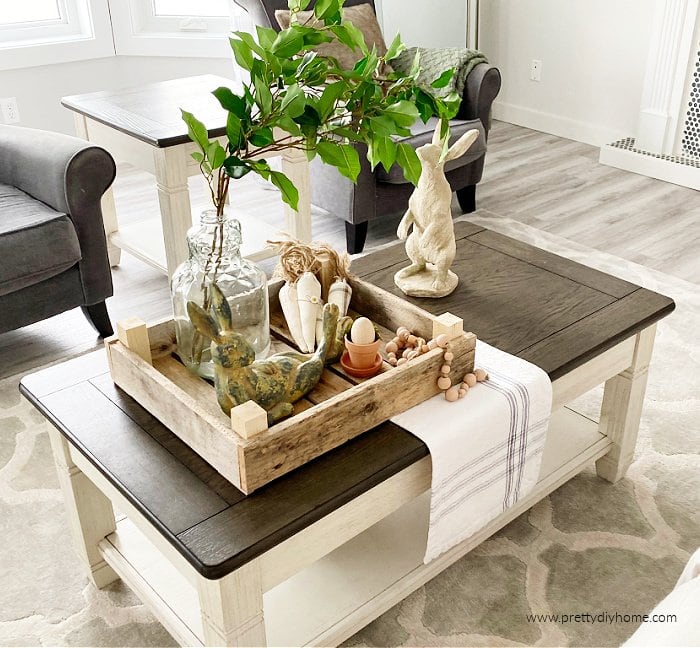 A coffee table decorated for Spring with a DIY tulip crate made from pallet wood. The tulip crate is holding an assortment of neutral Spring decor.