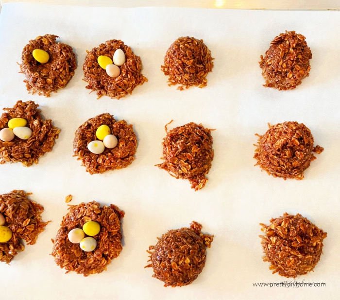 A parchment lined cookie sheet covered with birds nest Easter cookies. Half of the chocolate cookies are decorated to look like birds nests with mini chocolate Easter eggs, the remaining cookies are waiting their turn.