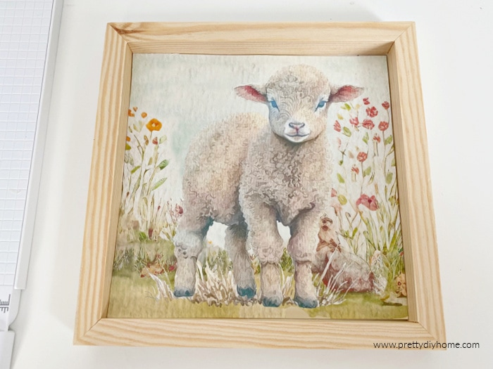 A Spring printable on canvas paper of a baby lamb and flowers. The wood sign craft has a natural wood frame.