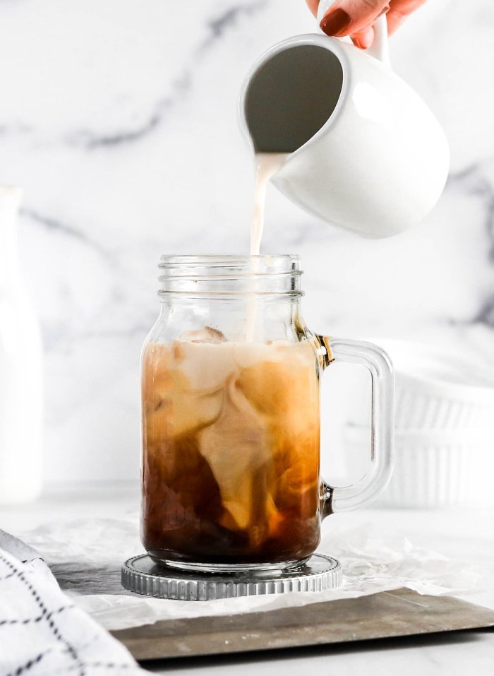 Almond milk being poured into an icy mug filled with espresso while making an almond latte.