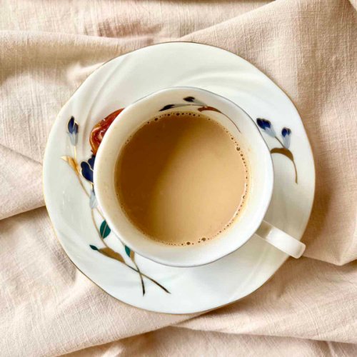 A tea cup and saucer shot from above so you can see the top of the tea cup. It is filled with a soft cream coloured yuanyang coffee.