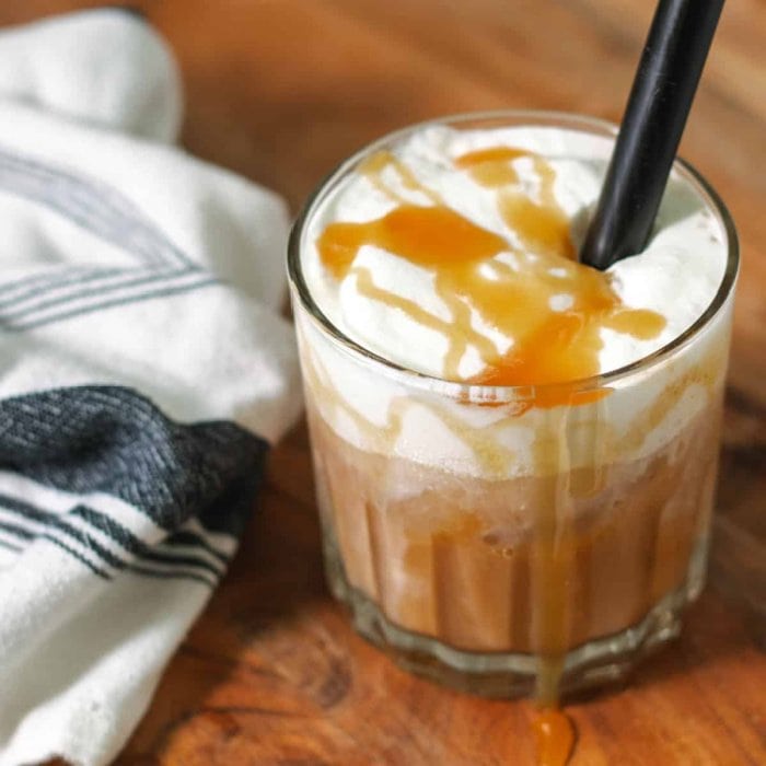 A clear glass filled with layer blended coffee latte. You can see the coffee layer, a creamy foam layer, and a caramel drizzle.