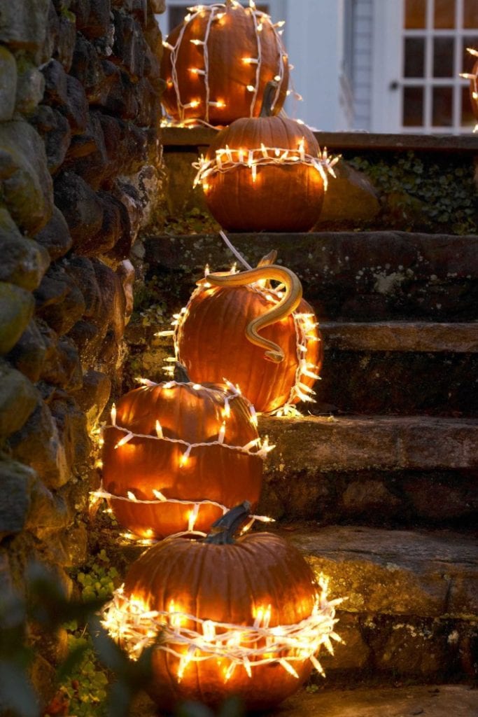 A cascading set of real pumpkins lined up on stairs. Each pumpkin is wrapped in warm white lights wrapped in a different direction.