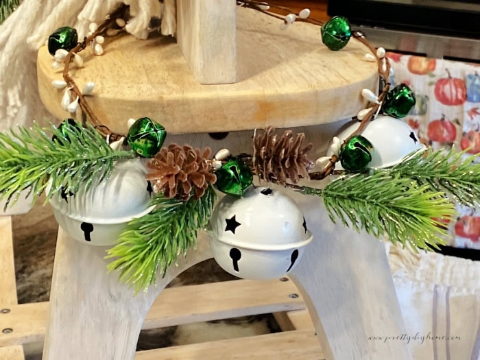 A cheerful wreath decoration for a Christmas decorated rocking horse.  The wreath is made with white sleigh bells, green jingle bells, pinecones and greenery.