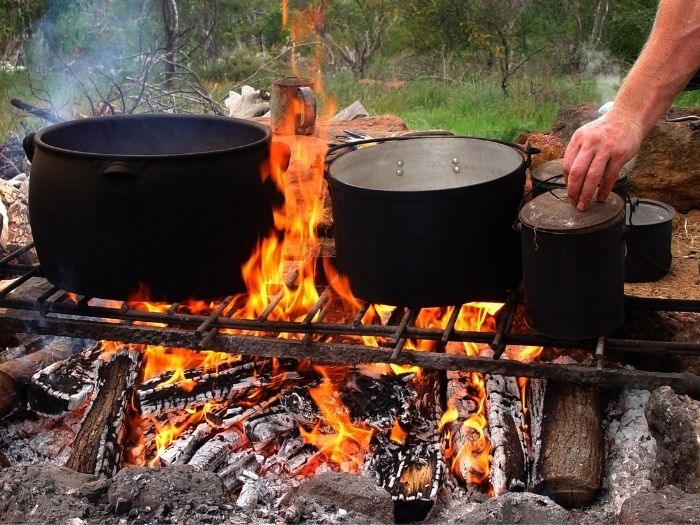 A burning campfire with a grill and several large black pots cooking food.