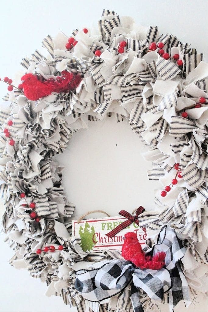 A large and fluffy rag wreath decorated for Christmas with red berries and a small red bird.