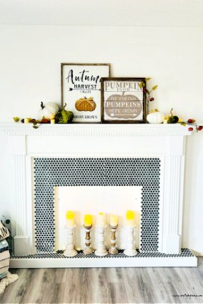 A DIY faux fireplace project made using a upcycles fireplace surround, and the mantel is decorated in Fall decor with pumpkin art, pumpkins and small bits of greenery.