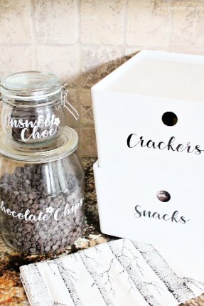 Two glass storage jars with chocolate chip and chocolate labels. And two white pantry boxes with Crackers and Snacks Labels